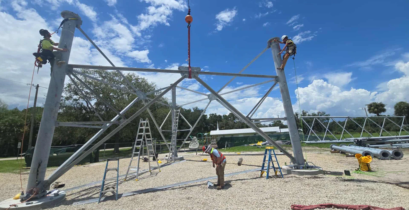 Vertical Axis crew erecting a self-supporting tower with a crane hook, climbers rigged off both legs, crew pad below