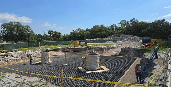 Vertical Axis crew setting the rebar cage and form boxes for a tower foundation, caution tape and dirt piles staged around the pad