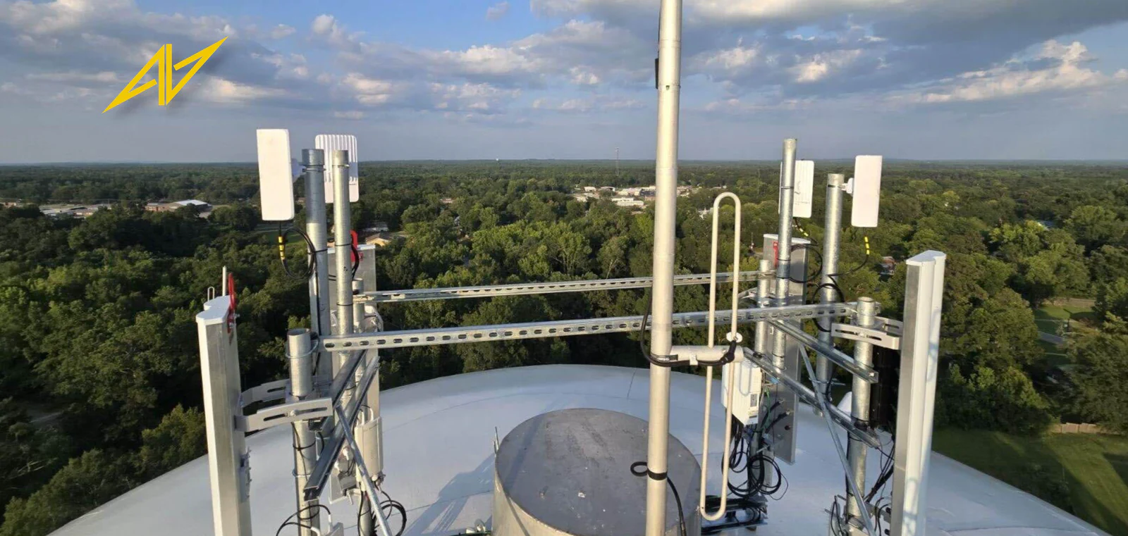 Aerial view of an Alabama Lightwave water-tower site with a full sector and backhaul array installed by Vertical Axis, Central Alabama treeline on the horizon