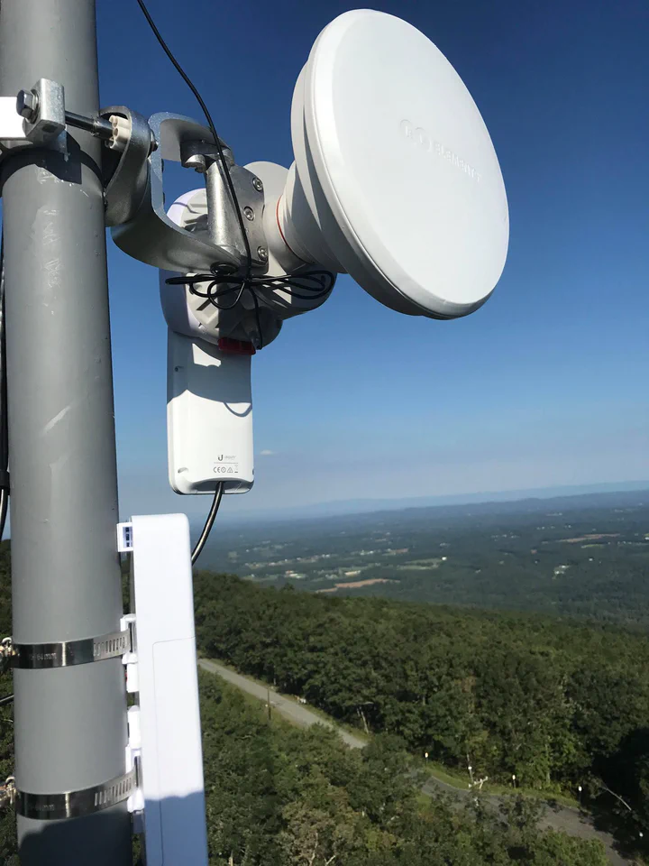 RF Elements horn antenna paired with a Ubiquiti radio on a tower pipe, dressed jumpers and cabling, rolling forest and farmland horizon stretching to the distance below