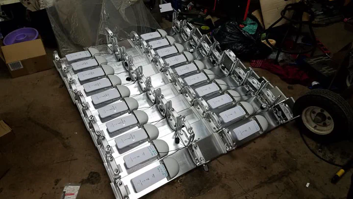 Workshop staging of a bulk radio rollout: dozens of PTP and CPE radios racked on galvanized shipping frames, serial numbers marked, pre-tested and ready for a program dispatch