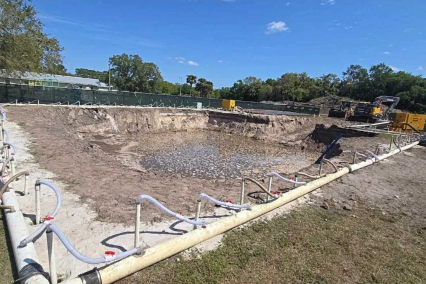 Formed-up tower foundation pit with grounding ring conduit running the full perimeter and concrete pipes staged along the edge