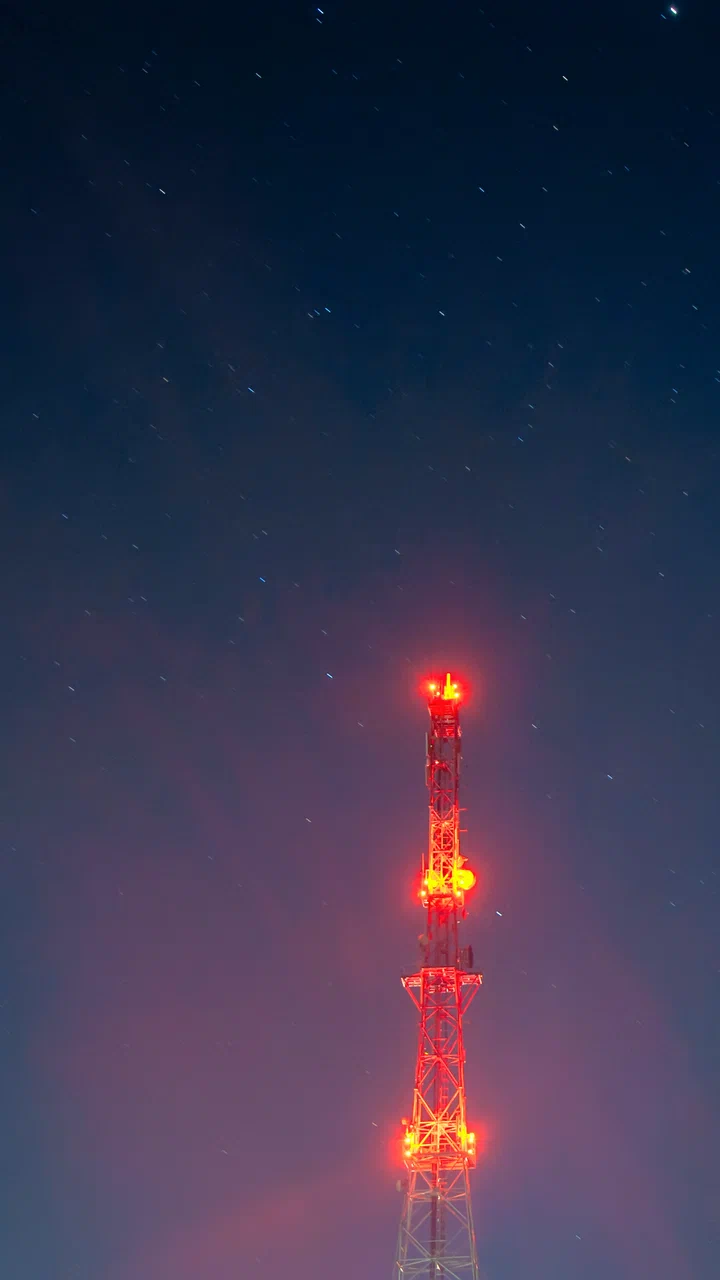 Tower silhouette under a starry night sky with red obstruction lights glowing