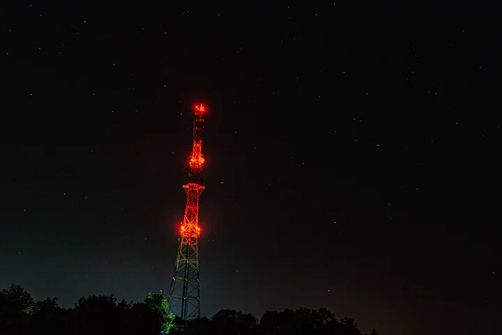 Communications tower at night with obstruction beacons lit against the sky
