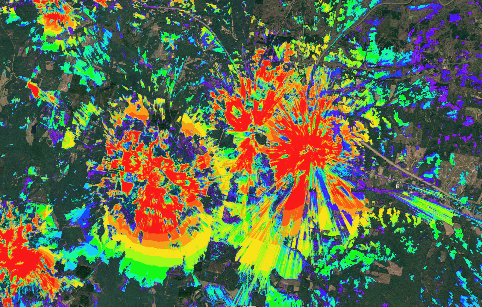 Vertical Axis RF propagation coverage model: two tower sites with red, orange, yellow, green, and blue signal-strength heatmaps overlaid on satellite imagery, showing the coverage footprint designed against the local terrain