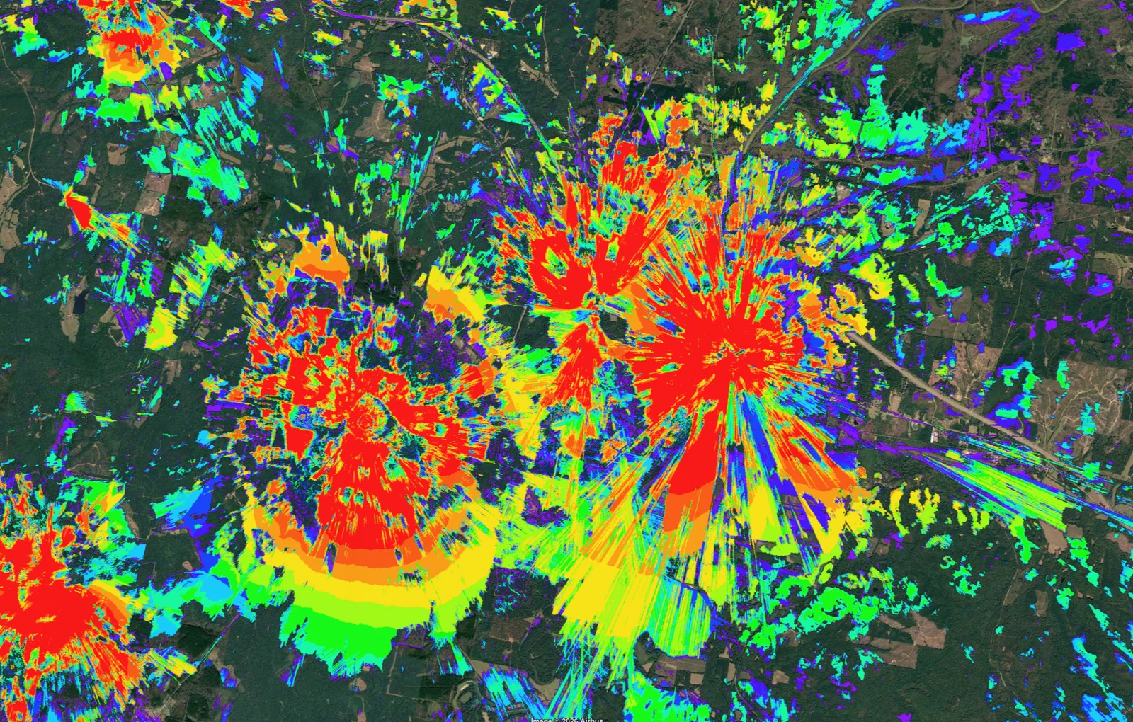 Vertical Axis RF propagation coverage model: two tower sites with red, orange, yellow, green, and blue signal-strength heatmaps overlaid on satellite imagery, showing the coverage footprint designed against the local terrain