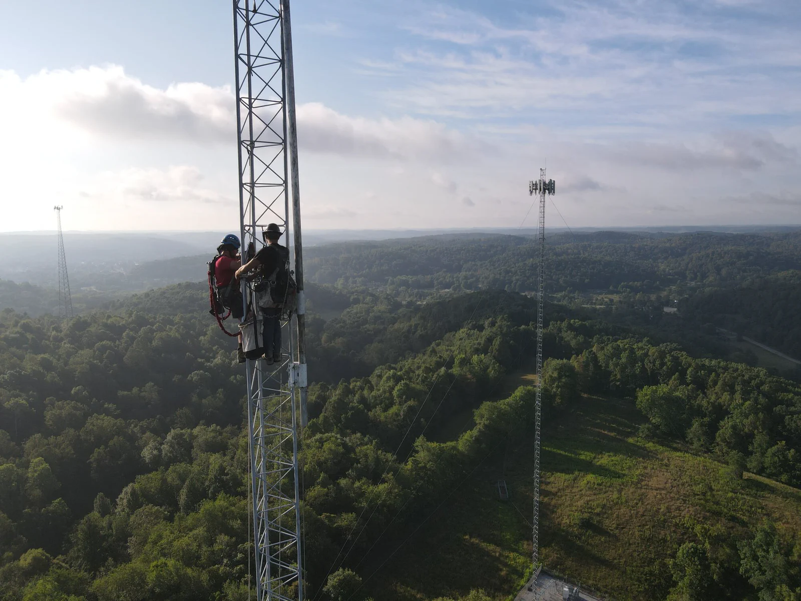 Vertical Axis climbers on a lattice tower, lower-48 landscape behind them